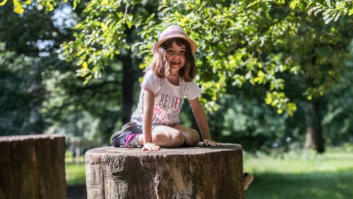 Girl sat on a log in the Log Pile play area at Dunham Massey, Cheshire